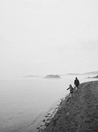 Parent child walking on the beach with view of sea against sky