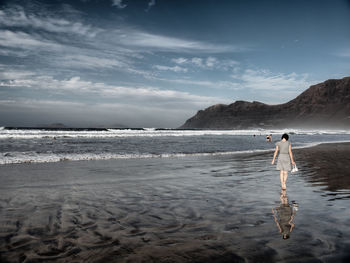 Rear view of woman waking on shore at beach against sky