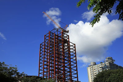 Low angle view of crane by building against blue sky