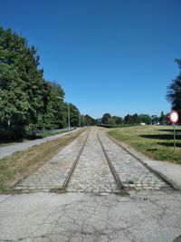 Railroad track amidst trees against clear blue sky