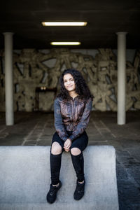 Full length portrait of teenage girl sitting on concrete at parking garage