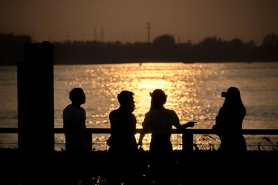 Silhouette people looking at sea against sky during sunset