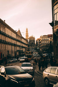 Vehicles on city street by buildings against sky