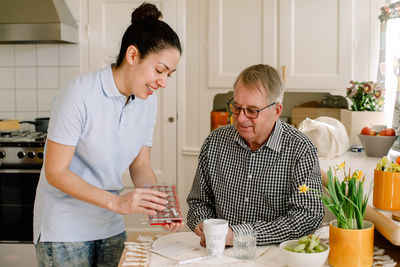 Smiling young female healthcare worker explaining medicines to retired elderly man sitting at table in nursing home