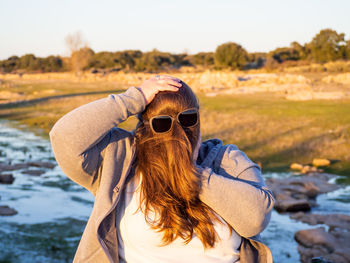 Woman with face covered by hair wearing sunglasses by stream