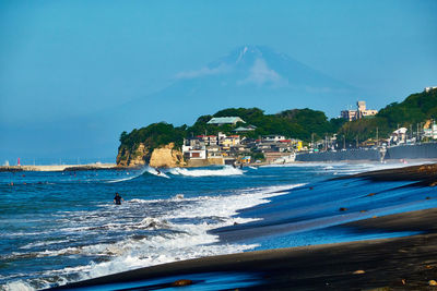 Scenic view of beach by buildings against blue sky