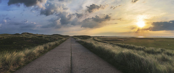 Empty road amidst field against sky during sunset