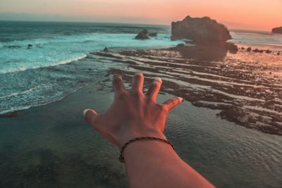 Cropped hand reaching sea during sunset