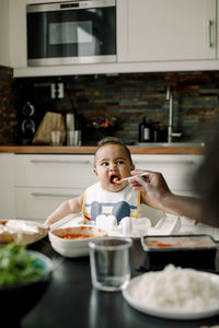 Cropped image of father feeding baby boy at dining table in kitchen