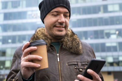 Millennial casual hipster man wear black hat using smartphone, standing outdoors at city street