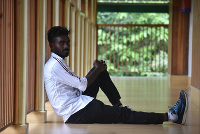 Side view of young man looking away while sitting on floor at home