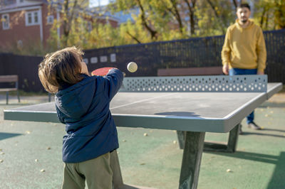Boy playing tablet tennis with father at park on sunny day
