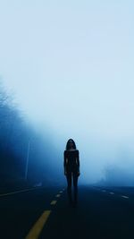 Rear view of woman walking on road in foggy weather