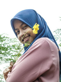 Portrait of beautiful young woman standing by flowering plants