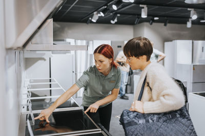 Saleswoman advising mature woman in buying modern appliance at electronics store