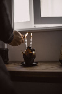 Woman lighting candles on cake at window sill