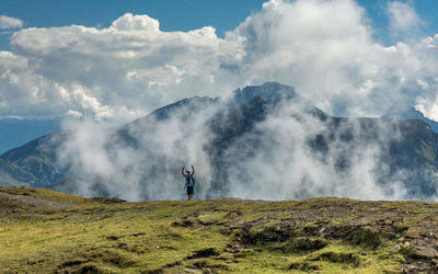 Excited man standing on mountain peak against sky