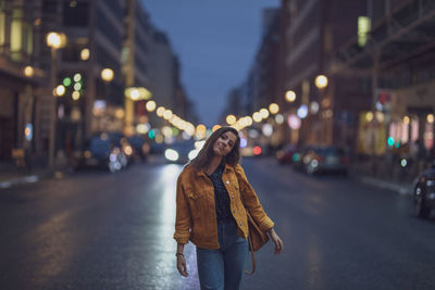 Portrait of young woman standing on road in city at night