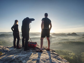 Three friends photographers discuss and taking photo from sticking out rock above misty pandscape