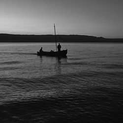 Silhouette people on boat in sea against sky