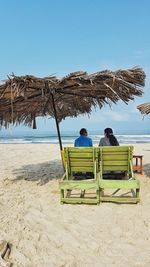 Rear view of men sitting on beach against clear sky