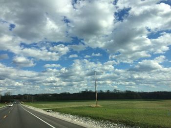 Road passing through field against cloudy sky