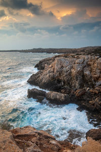 Rocks on sea shore against sky during sunset