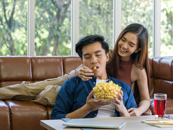 Young woman eating food while sitting on sofa