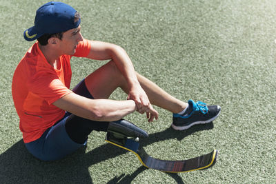 Full length of athlete with prosthetic leg sitting on field against sky