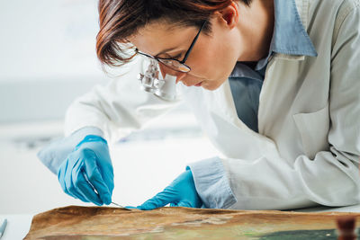 Professional painting conservator uses scalpel to carefully remove patches from an oil painting