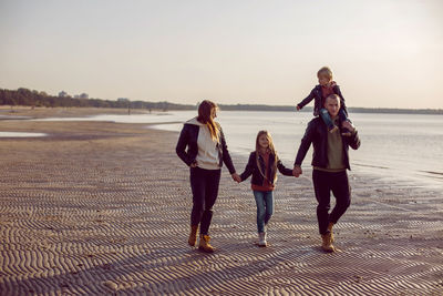 Family in a leather jacket walks along the beach with their dog in autumn