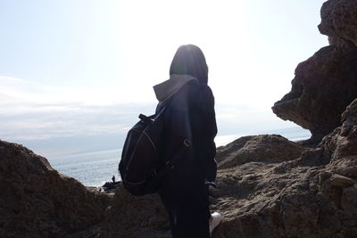 Rear view of woman standing on cliff by sea