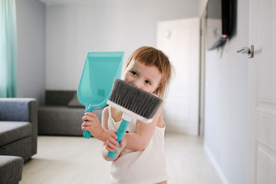 Cute european child with blue scoop for garbage and brush for sweeping floor helps to clean