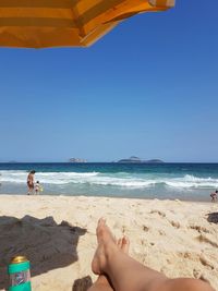 Low section of person resting at beach against clear blue sky