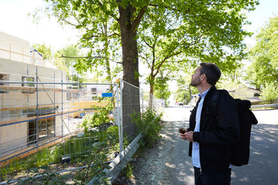 Businessman looking at incomplete building while standing on street during sunny day