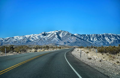 Road by snowcapped mountains against clear blue sky