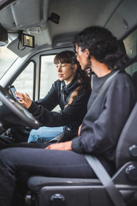 Female mover showing mobile phone to coworker while sitting in truck
