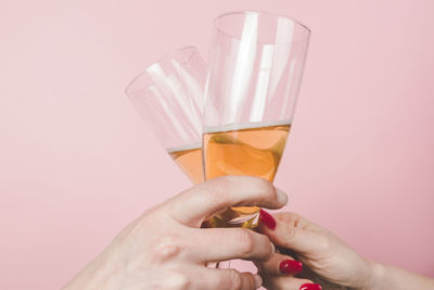 Cropped hands of friends toasting champagne flutes against pink background