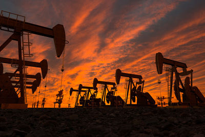 Silhouette oil pumps on field against cloudy sky during sunset