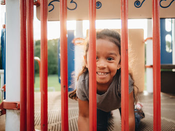 Portrait of cute girl sitting by gate outdoors
