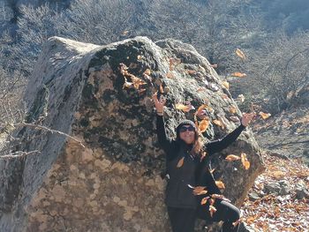 Woman throwing leaves while standing on land against rock