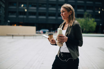 Mature businesswoman carrying food and drink with laptop while walking on footpath in city