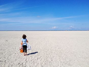 Rear view of boy on beach against sky on sunny day