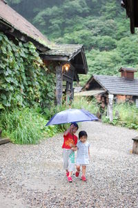 Siblings walking with umbrella on road in village