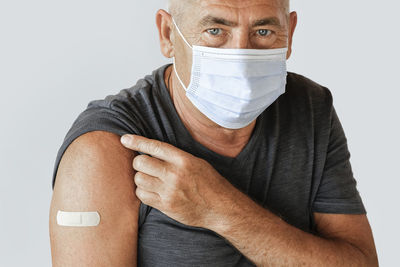 Senior man showing arm with bandage. vaccine covid 19, pox, monkeypox vaccination. gray background.