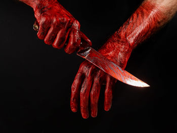 Cropped hand of person holding knife against black background