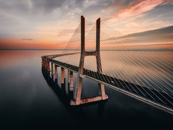 Bridge over calm sea against sky during sunset