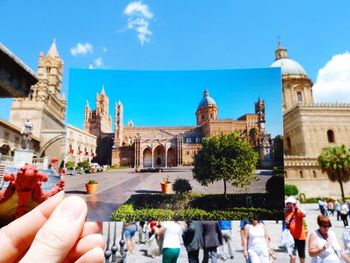 Cropped image of hand holding photograph against palermo cathedral