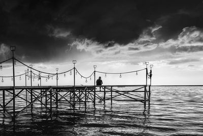 Man sitting on pier over sea against sky