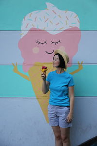 Woman holding ice cream cone while standing against mural wall